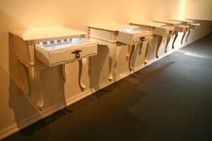 Foto sala da exposição de Gilberto Freyre onde há criados mudos com gavetas vitrines com objetos.
